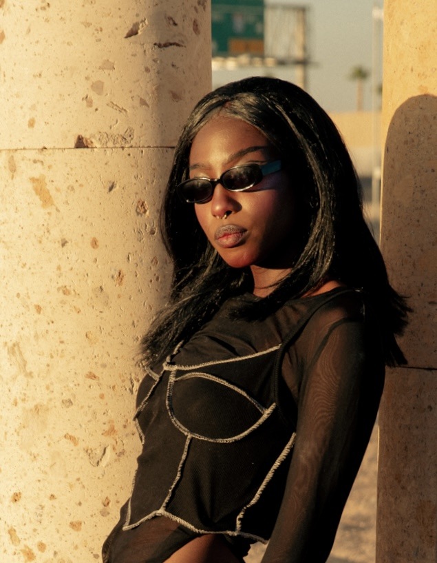 Golden-light fashion portrait wearing sunglasses beside pale stone columns
